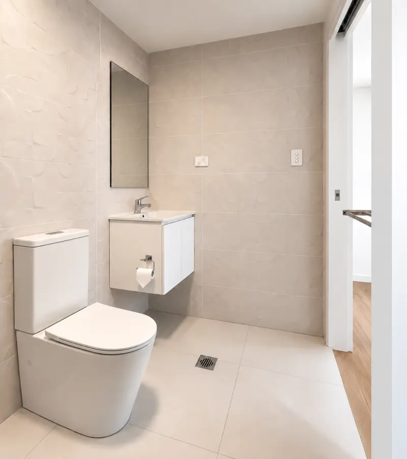 Compact tiled bathroom with a white vanity, toilet and walk-in shower